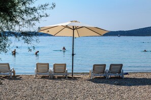 A pebbled beach with four lounge chairs and a large umbrella. - Hotel Miramare (Vodice)