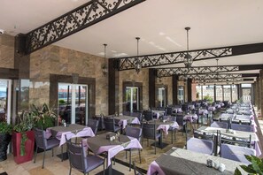 A spacious outdoor dining area with multiple tables and chairs, stone walls, and decorative metal railings. - Hotel Miramare (Vodice)