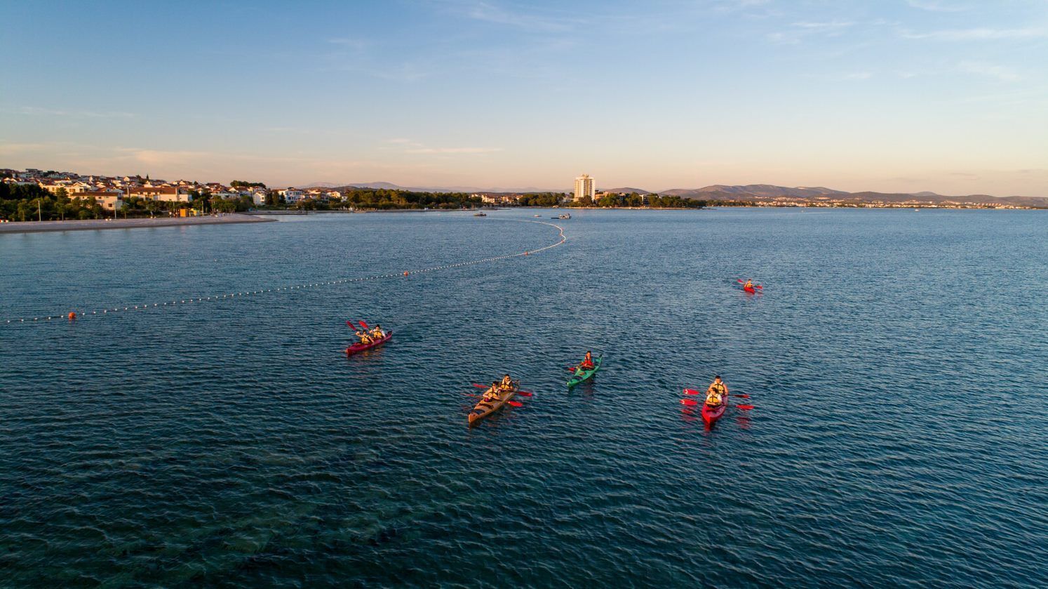 A calm body of water with kayaks and a distant cityscape.