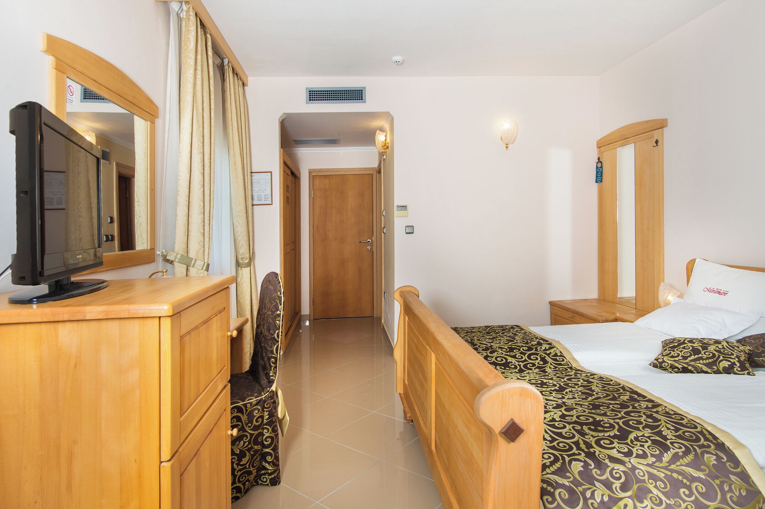 A hotel room with a wooden bed, a TV on a wooden dresser, and a mirror.