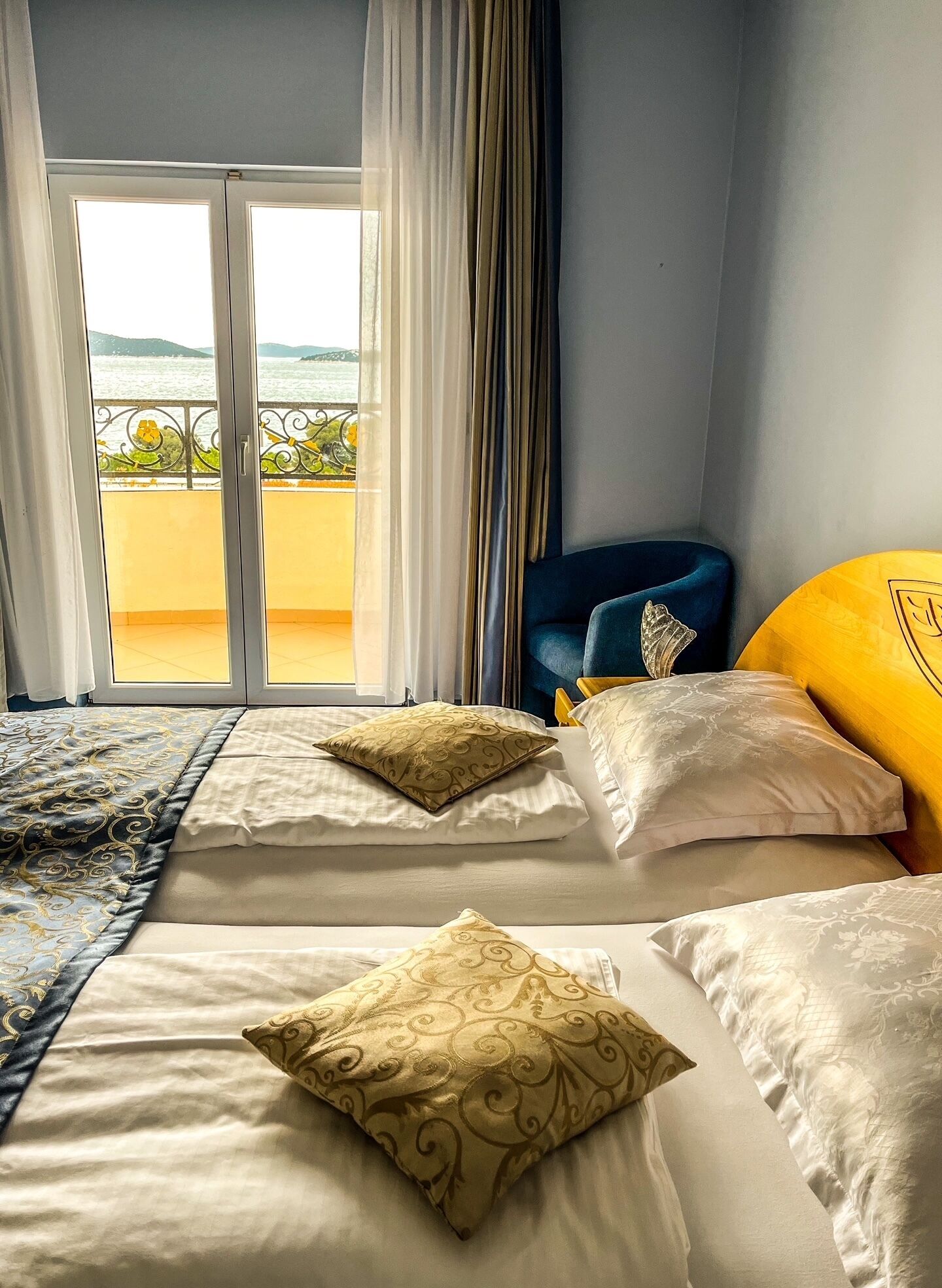 A hotel room with two beds, a view of the sea, and a balcony with a railing.