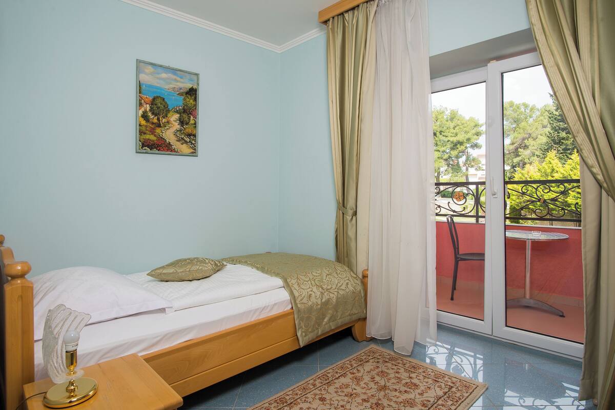 A bedroom with a bed, a nightstand, a painting on the wall, and a balcony with a chair and table.