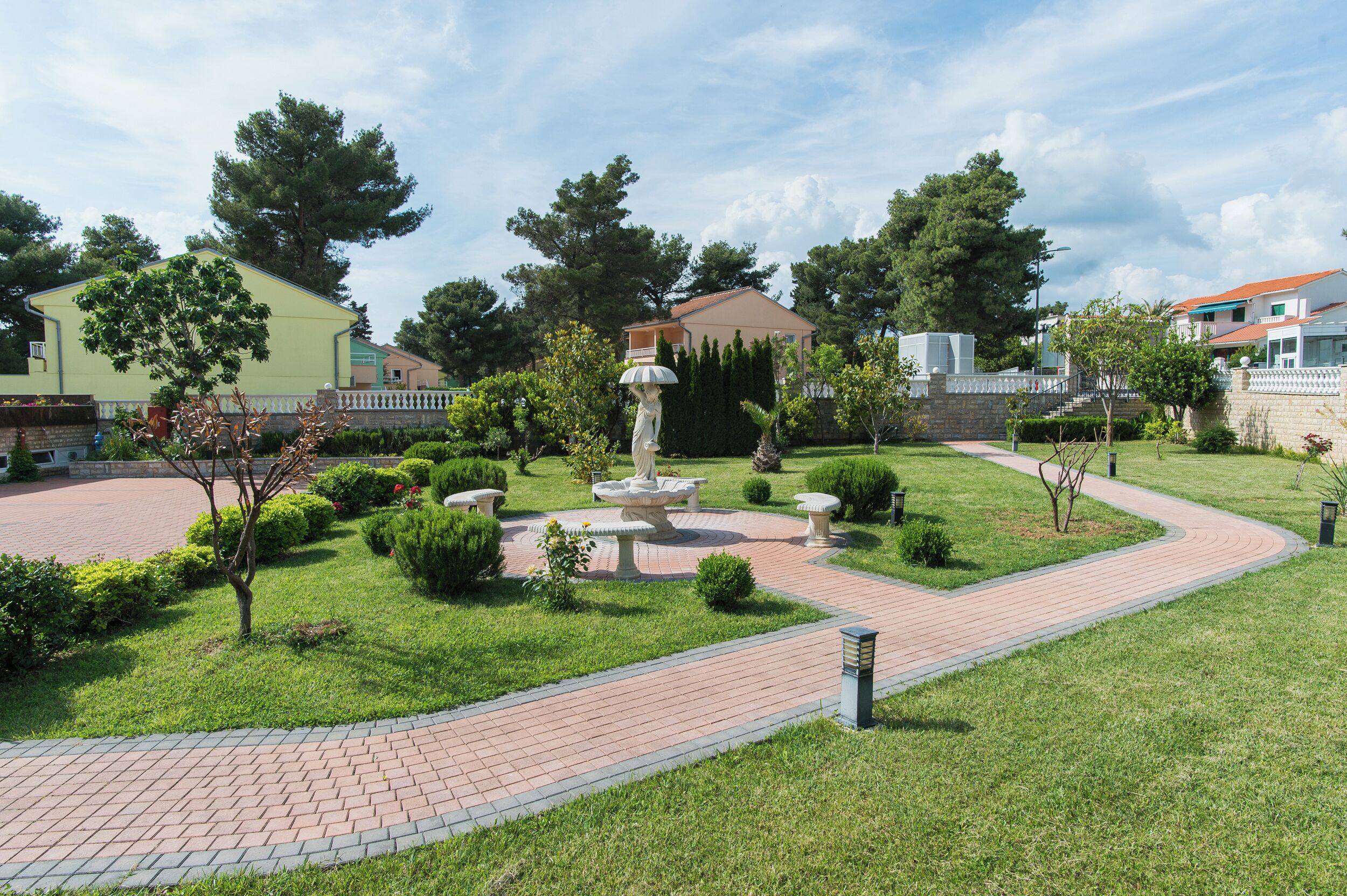 Jardí paisatjístic amb una font central, camins pavimentats i vegetació circumdant.