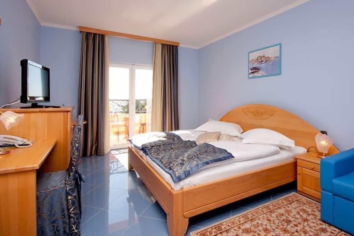 A hotel room with a bed, a desk, a chair, a television, and a balcony with curtains.
