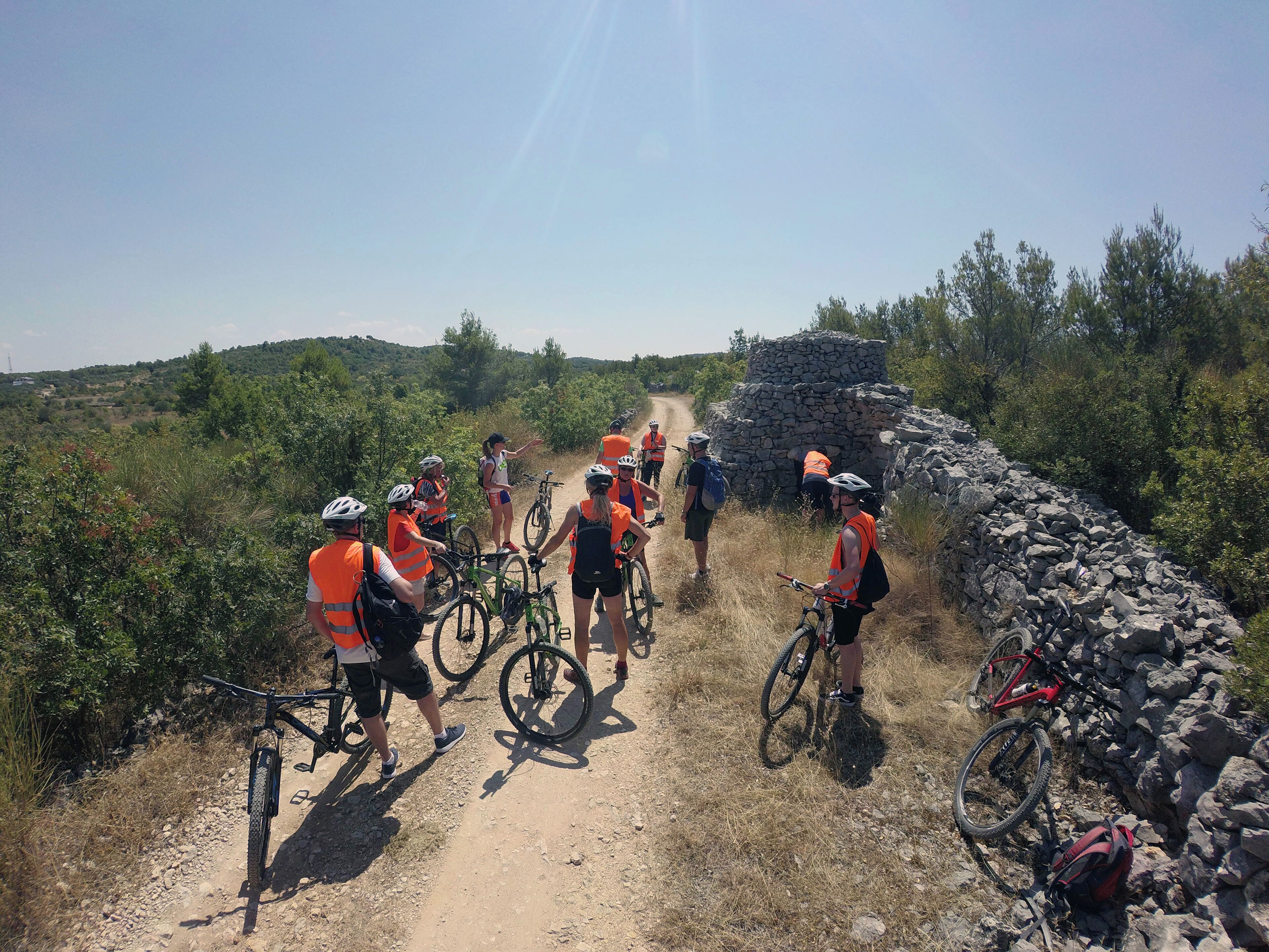 Een groep fietsers op een onverhard pad, met een stenen muur aan de ene kant en groen aan de andere kant.