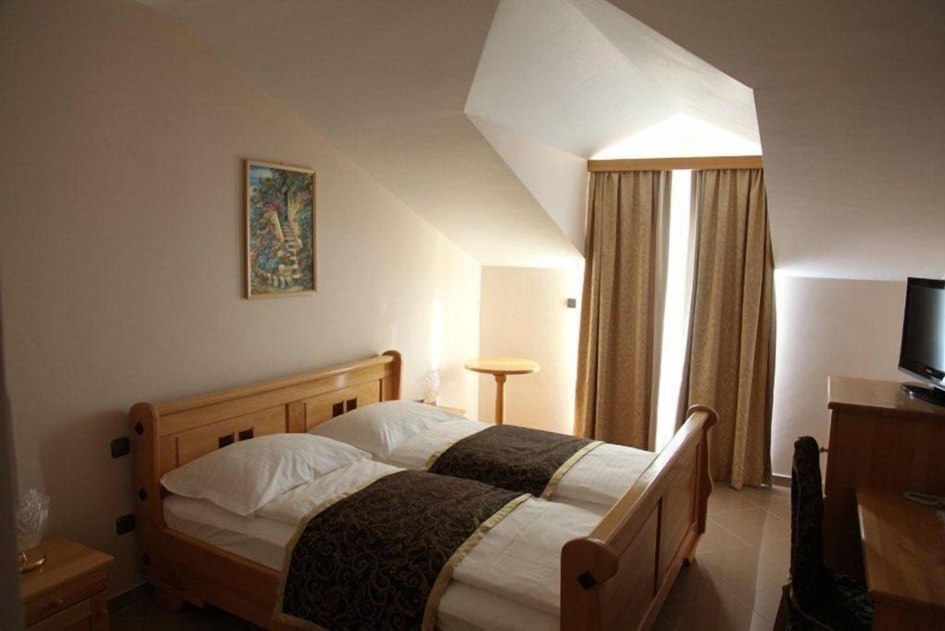 A hotel room with two wooden beds, a painting on the wall, a desk with a television, and a window with curtains.