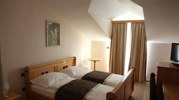 A hotel room with two wooden beds, a painting on the wall, a desk with a television, and a window with curtains.