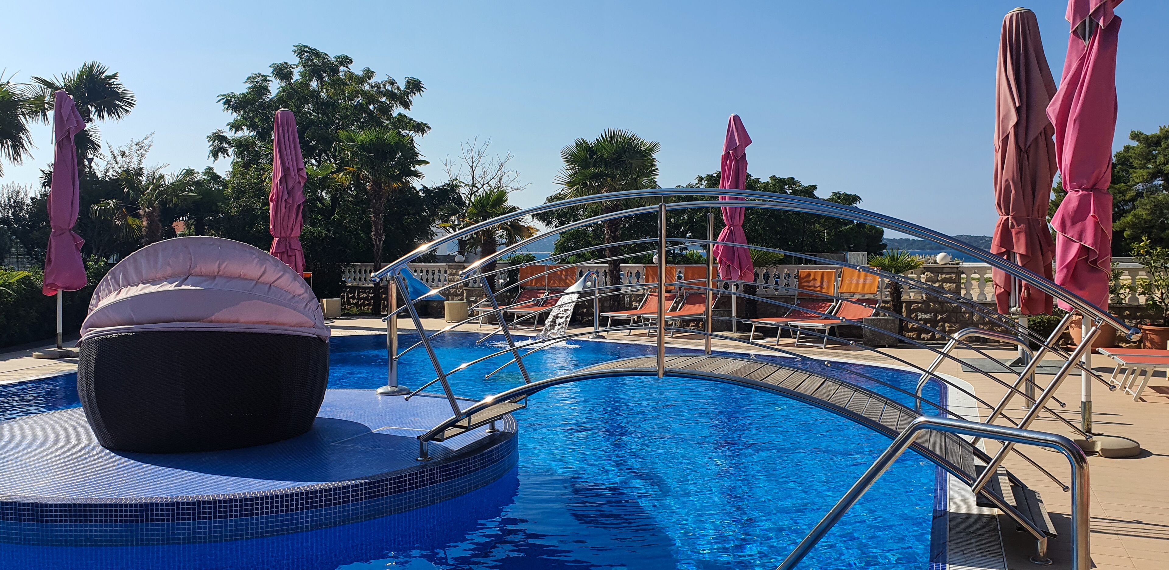 A swimming pool with a hot tub, lounge chairs, and umbrellas.