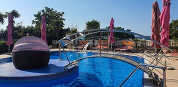 Une piscine avec un jacuzzi, des chaises longues et des parasols.