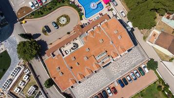 An aerial view of a building with a tiled roof, a swimming pool, and a parking lot.