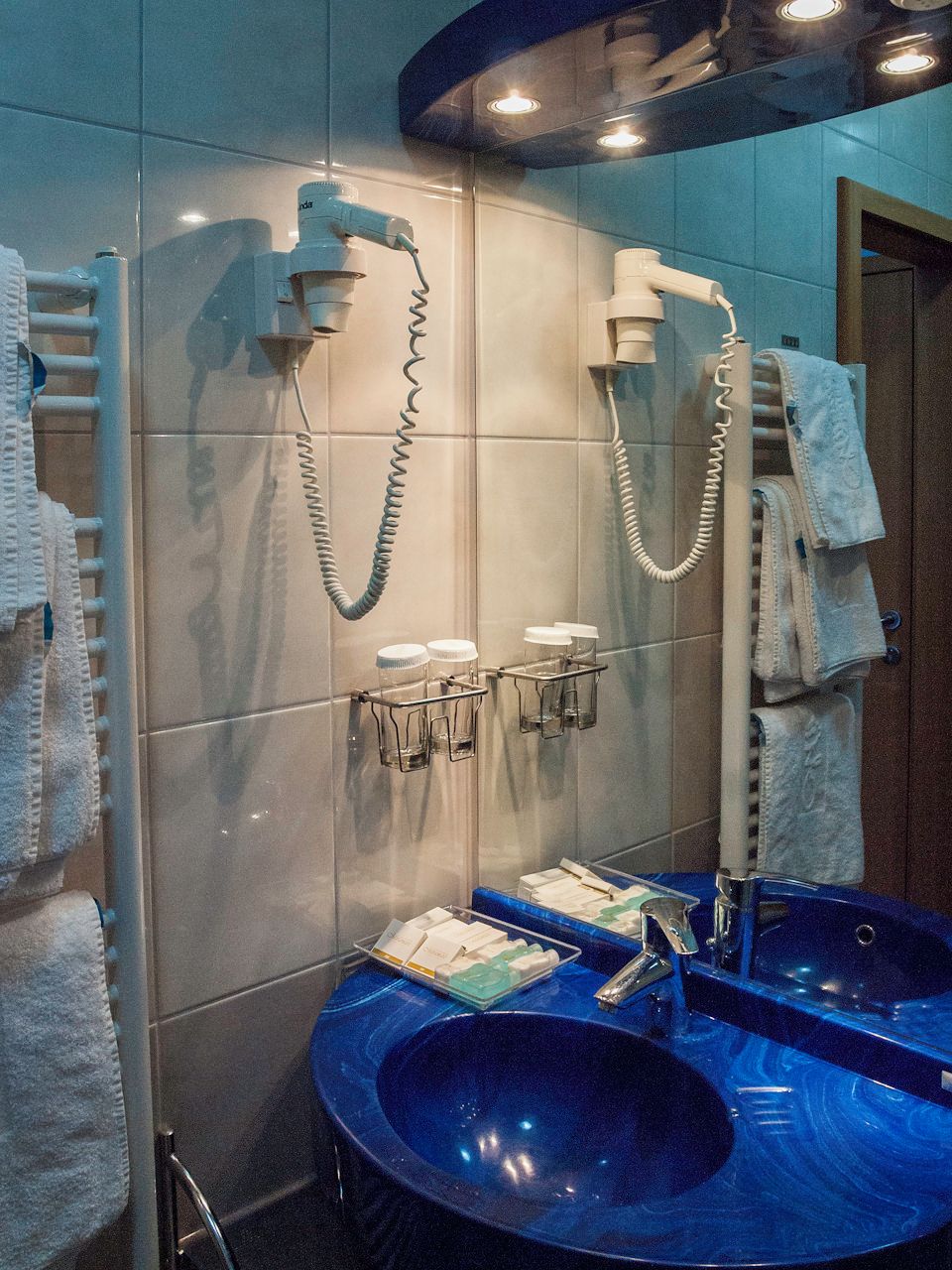Un baño con un espejo grande, dos lavamanos, toalleros y una zona de ducha.