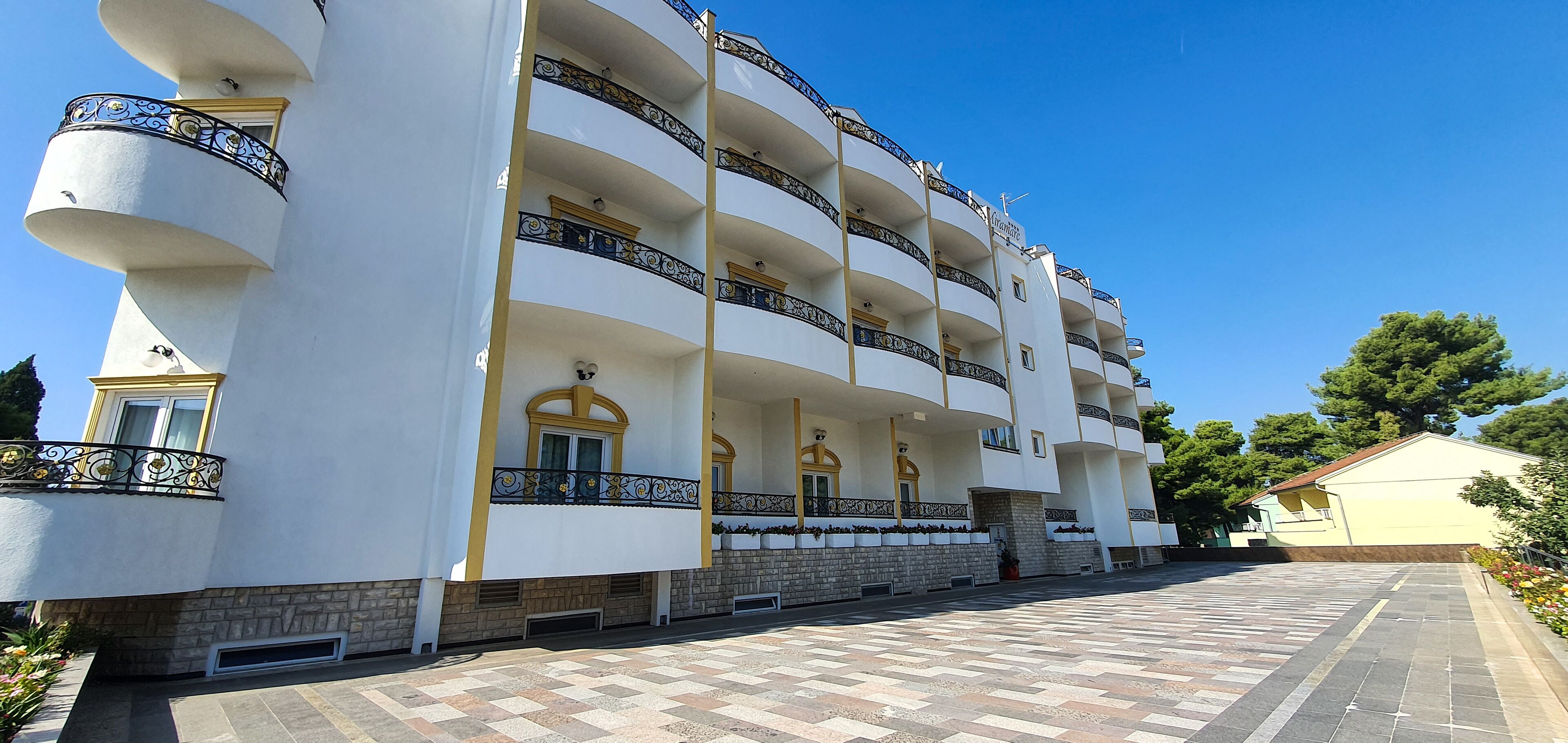 A multi-story hotel with balconies, a tiled entrance, and a clear sky.