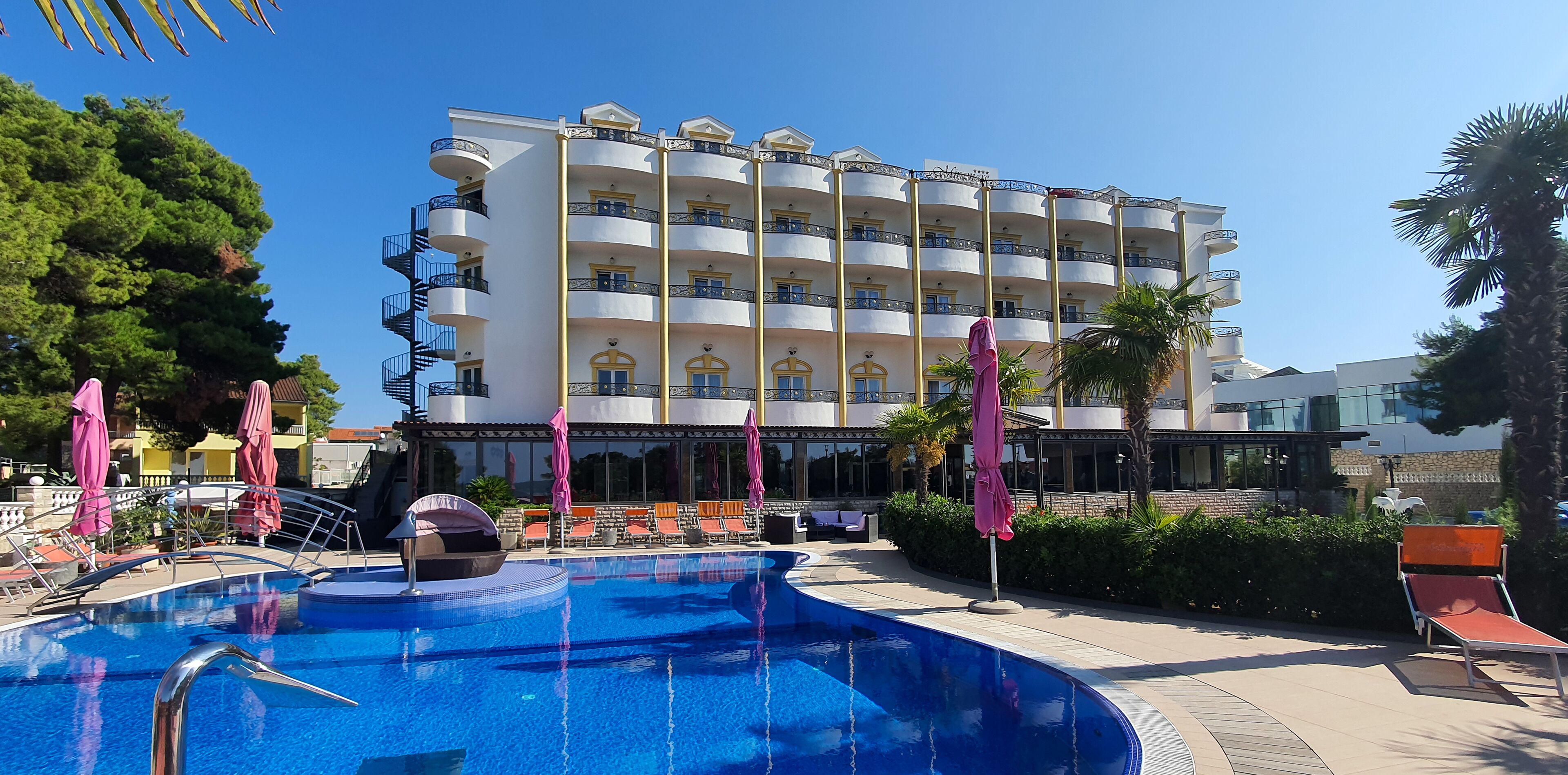 A hotel with a swimming pool, multiple balconies, and outdoor seating areas.