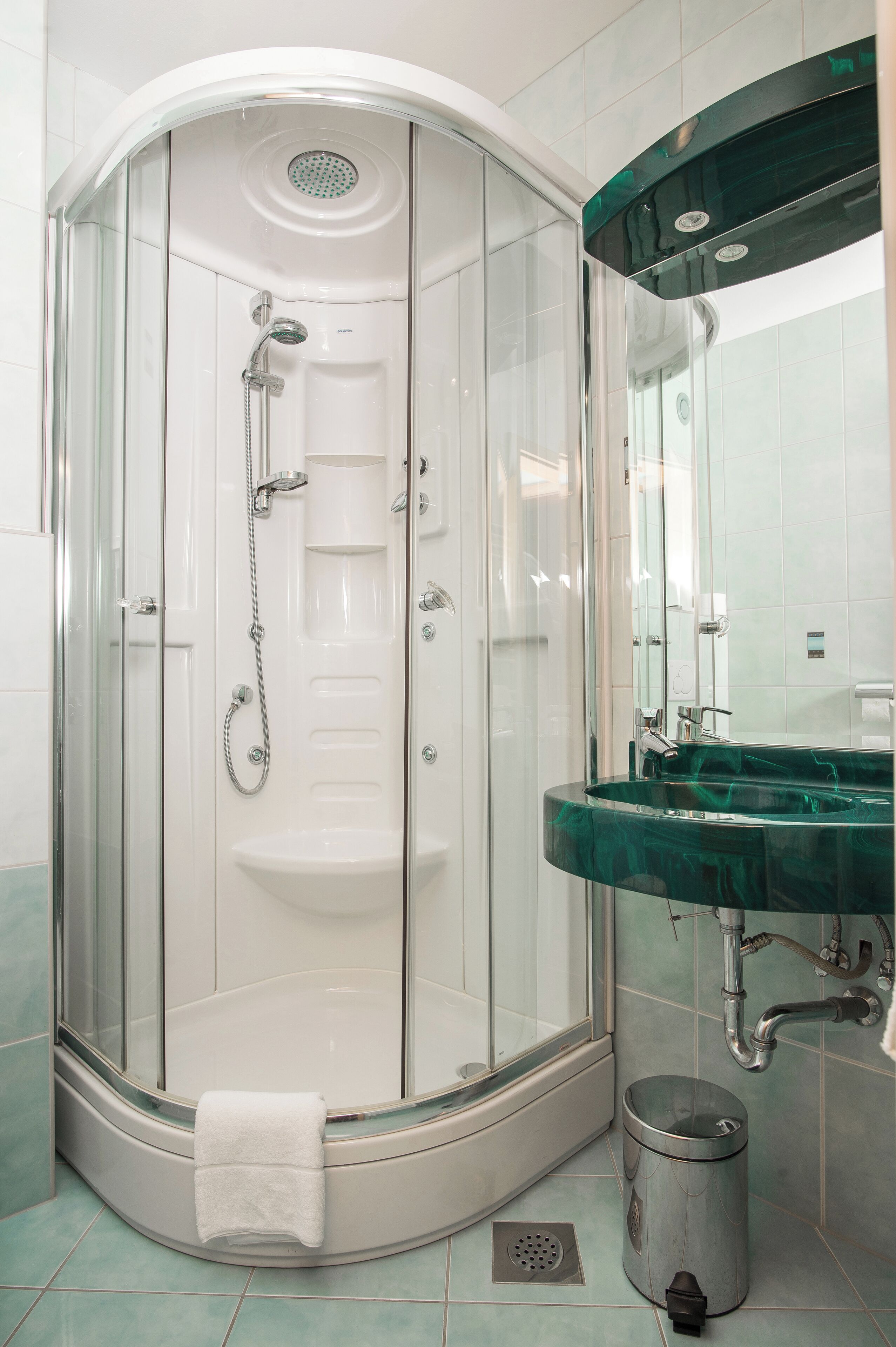A glass-enclosed shower with a white sink and a green marble countertop.