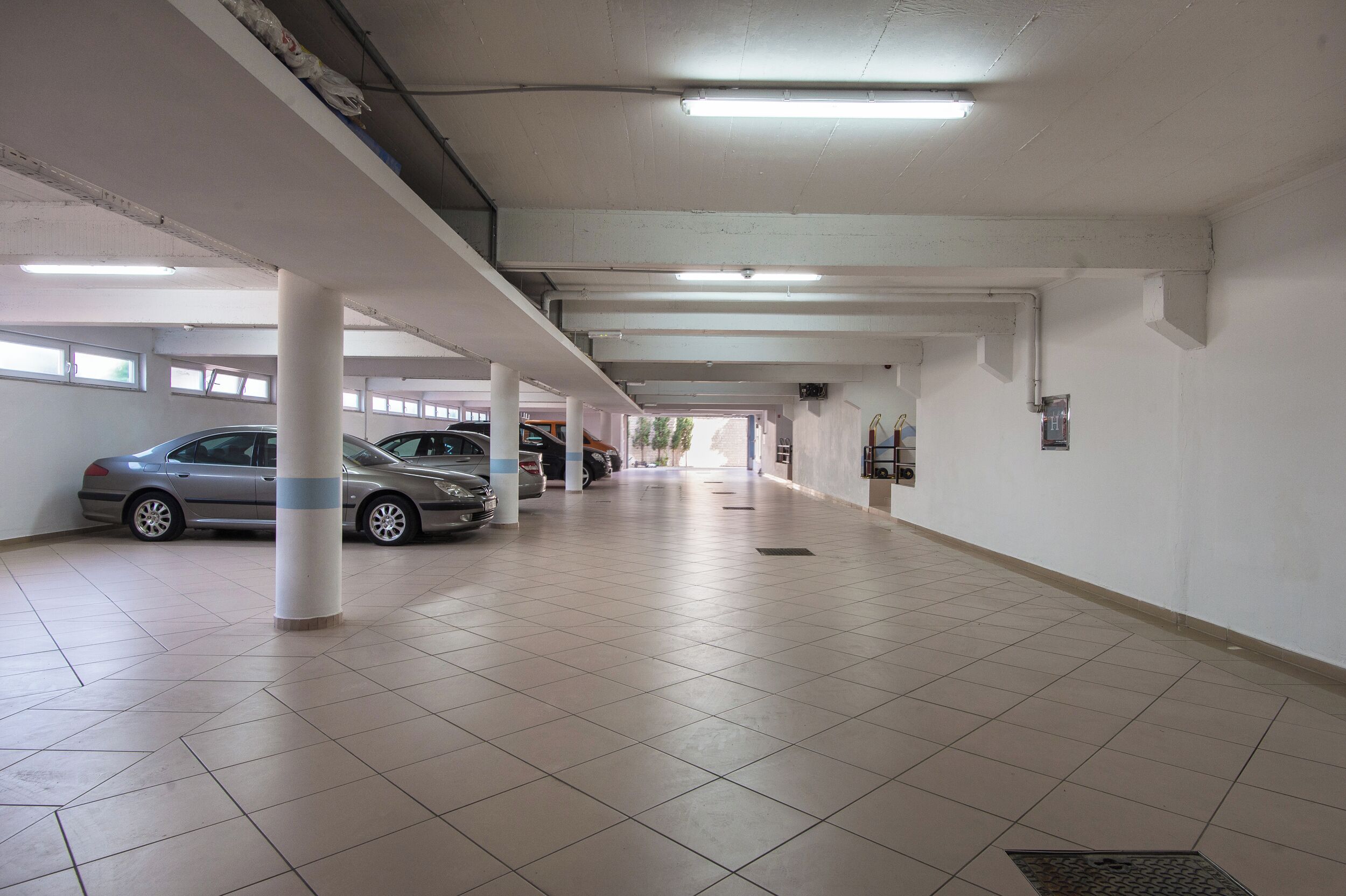A parking garage with multiple cars parked, white pillars, and fluorescent lighting.