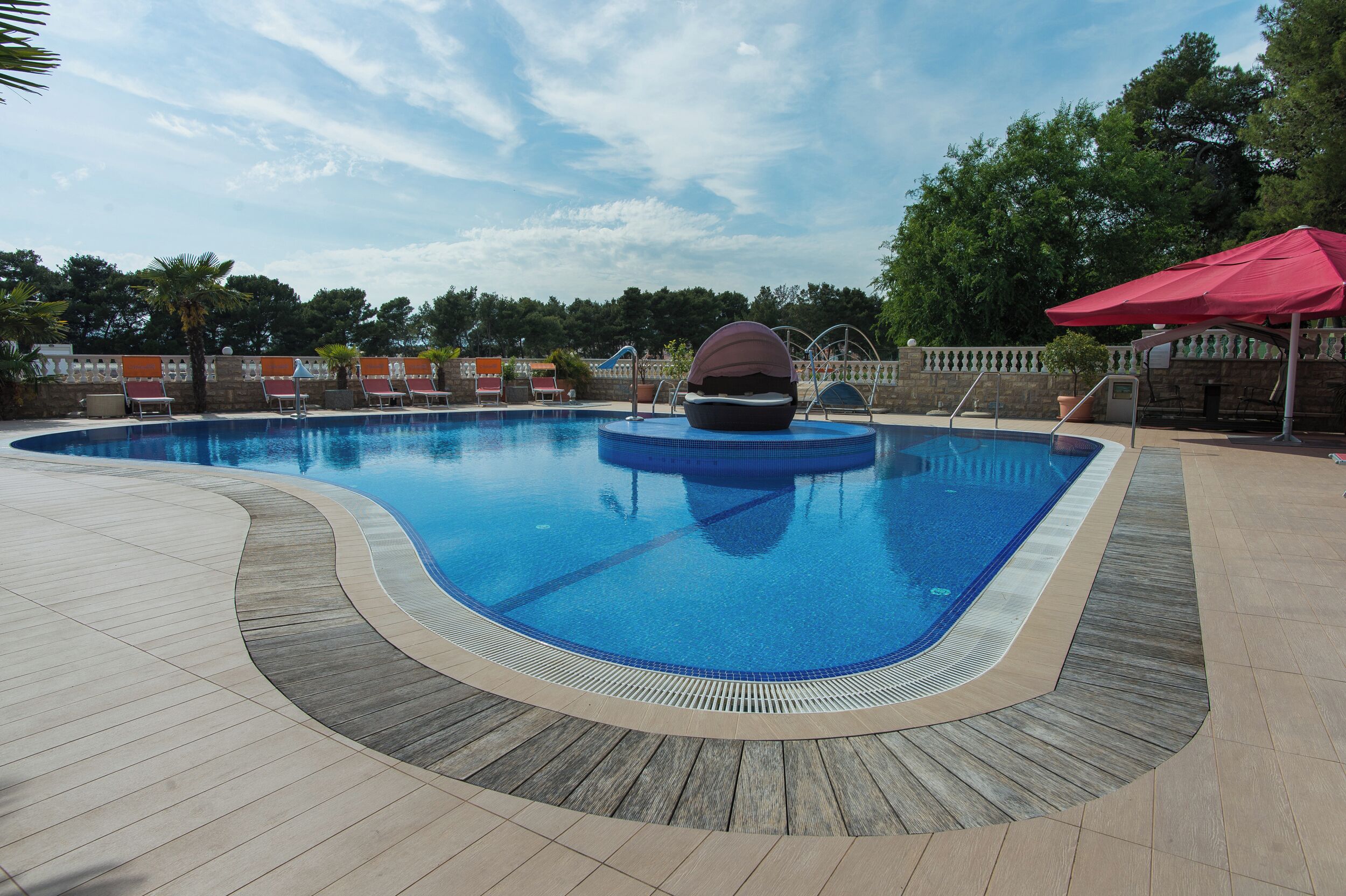 A swimming pool with a wooden deck, a hot tub, and a red umbrella.