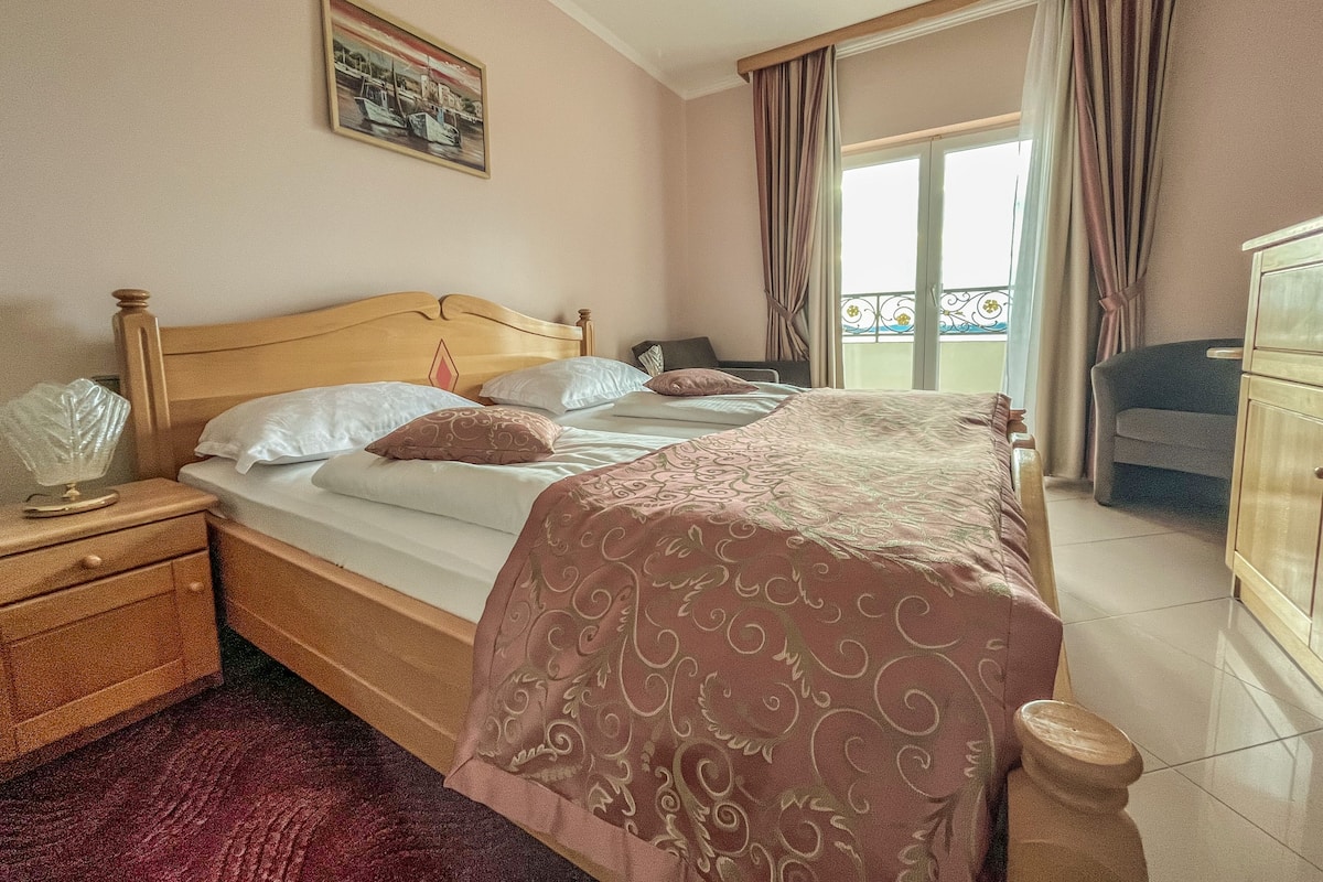A bedroom with a wooden bed, a nightstand, a dresser, and a balcony with curtains.