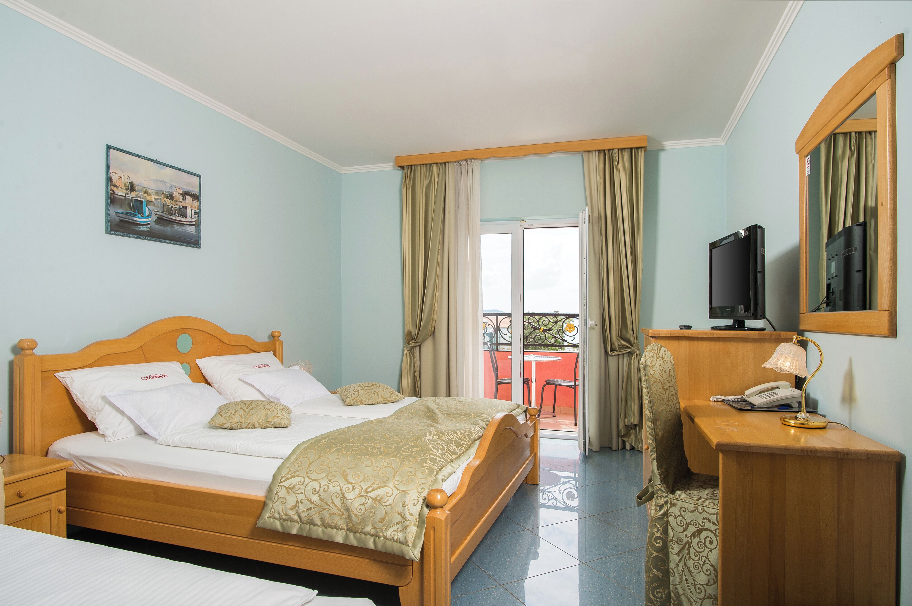 Ein Hotelzimmer mit Bett, Schreibtisch mit Telefon, Fernseher und Balkon mit Tisch und Stühlen.