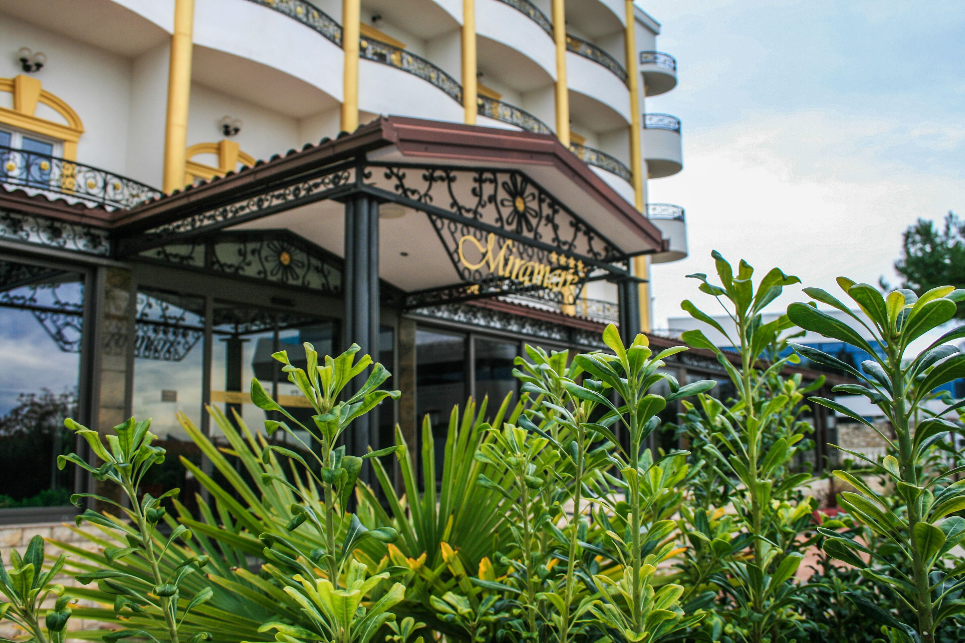A building with balconies, a covered entrance, and lush greenery in the foreground.