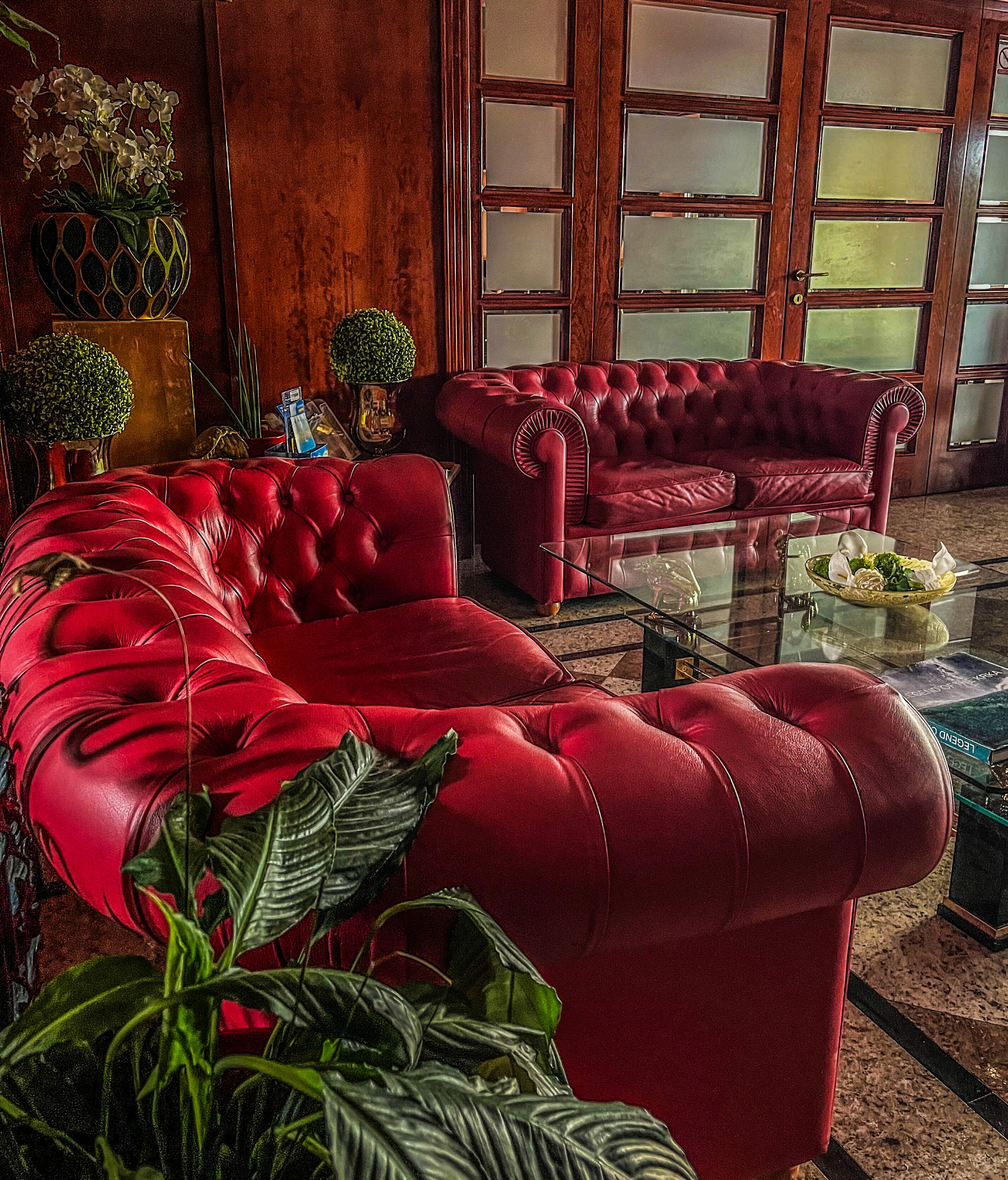 A spacious living room with a red leather sofa set, a glass coffee table, and various decorative items including a vase with flowers and a small potted plant.