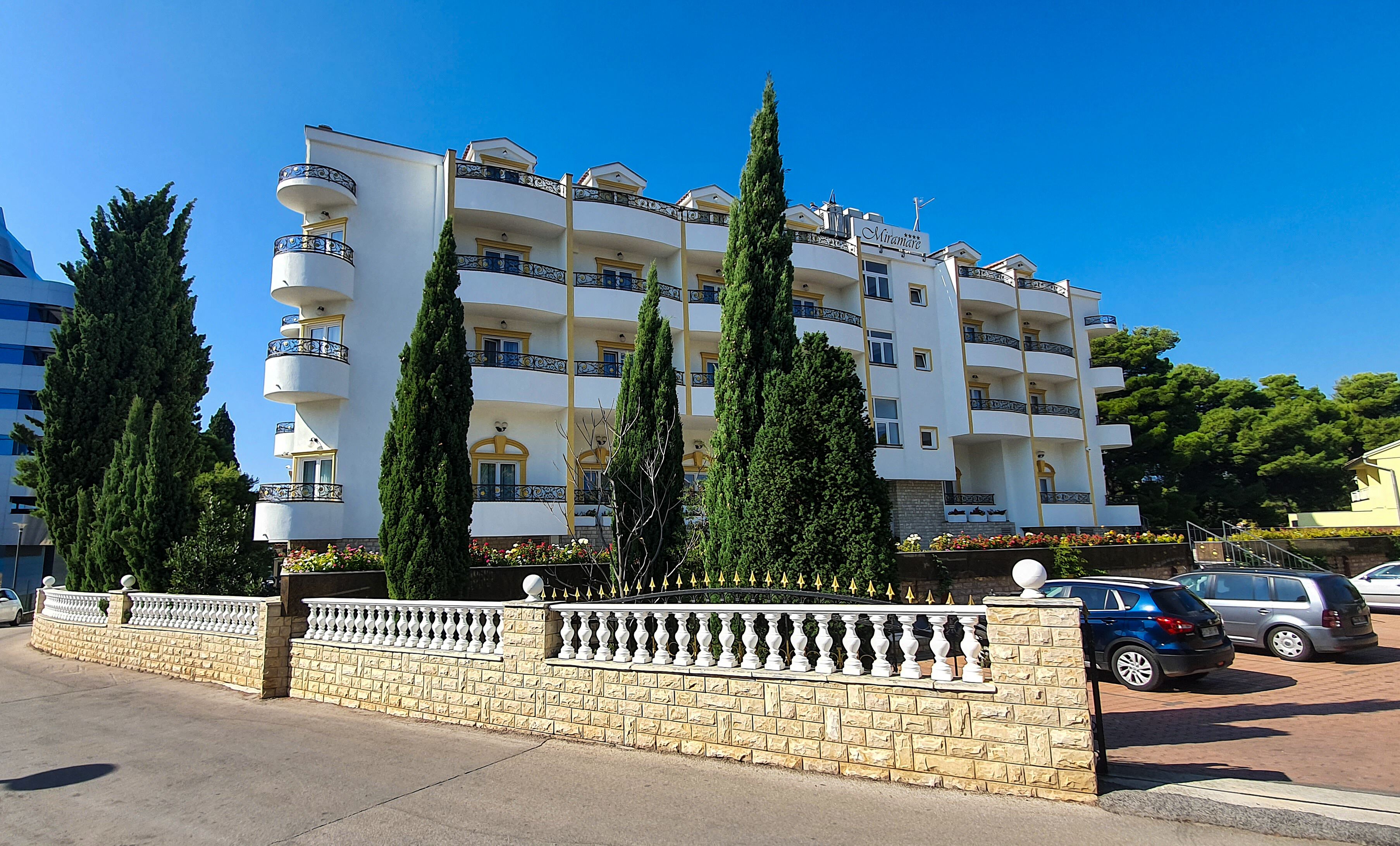 A multi-story hotel with balconies, a stone wall, and parked cars.