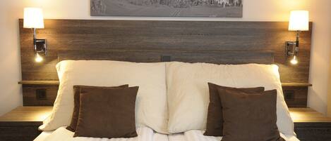Una cama doble con dos almohadas marrones, un cabecero de madera y dos lámparas fijadas a la pared.