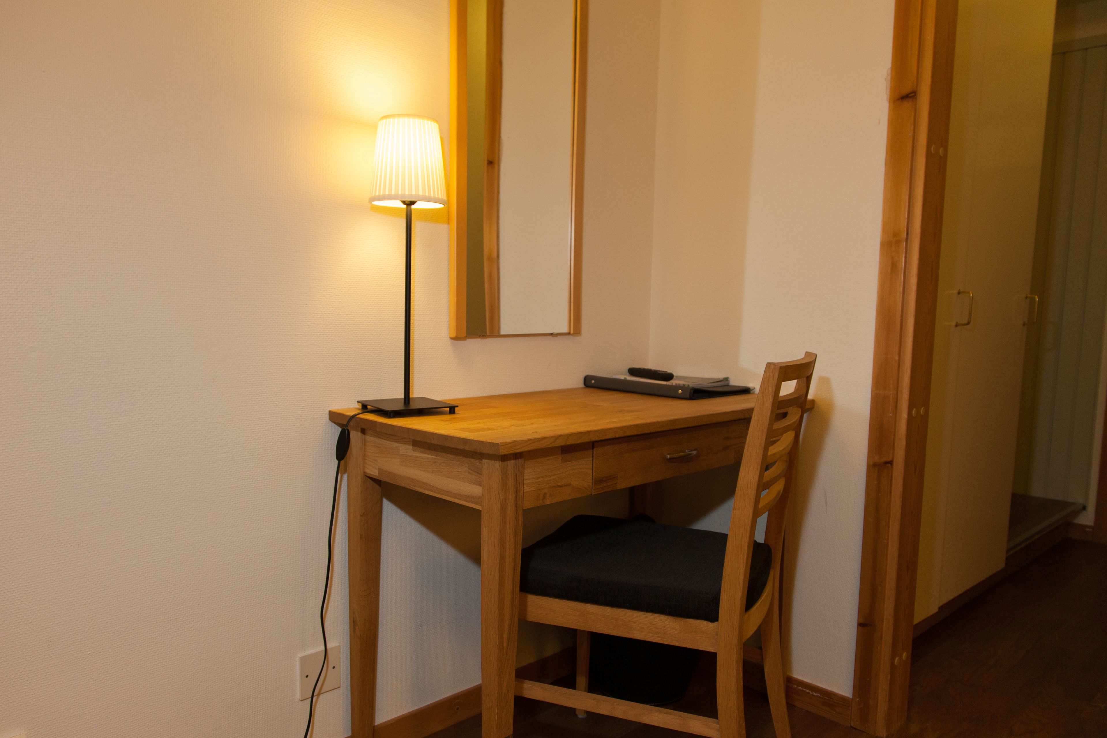 Un bureau en bois, une lampe, une chaise et un miroir.