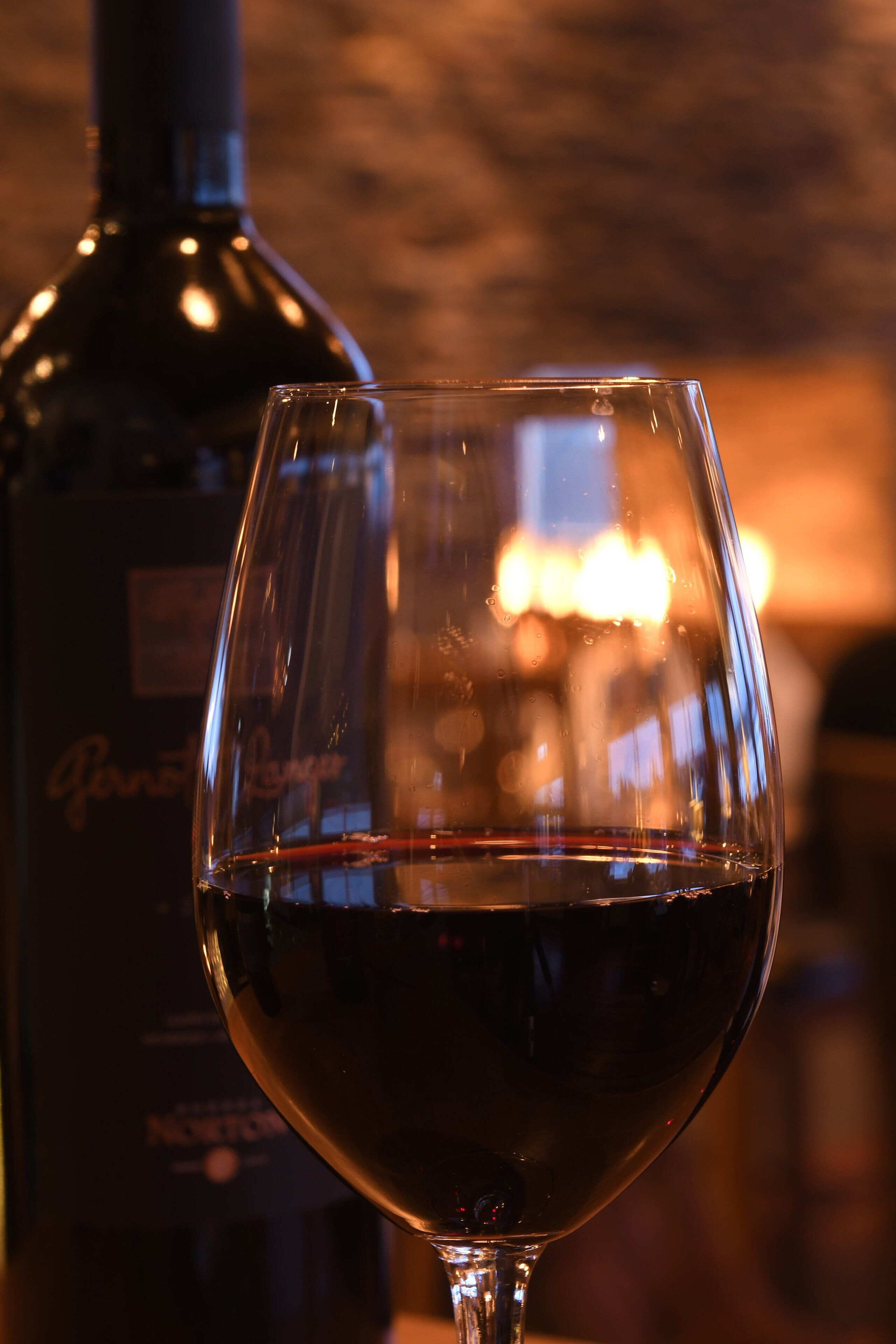 A glass of red wine with a bottle in the background.
