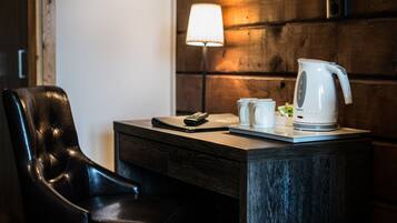 Un escritorio de madera con un hervidor eléctrico blanco, un control remoto y una libreta.