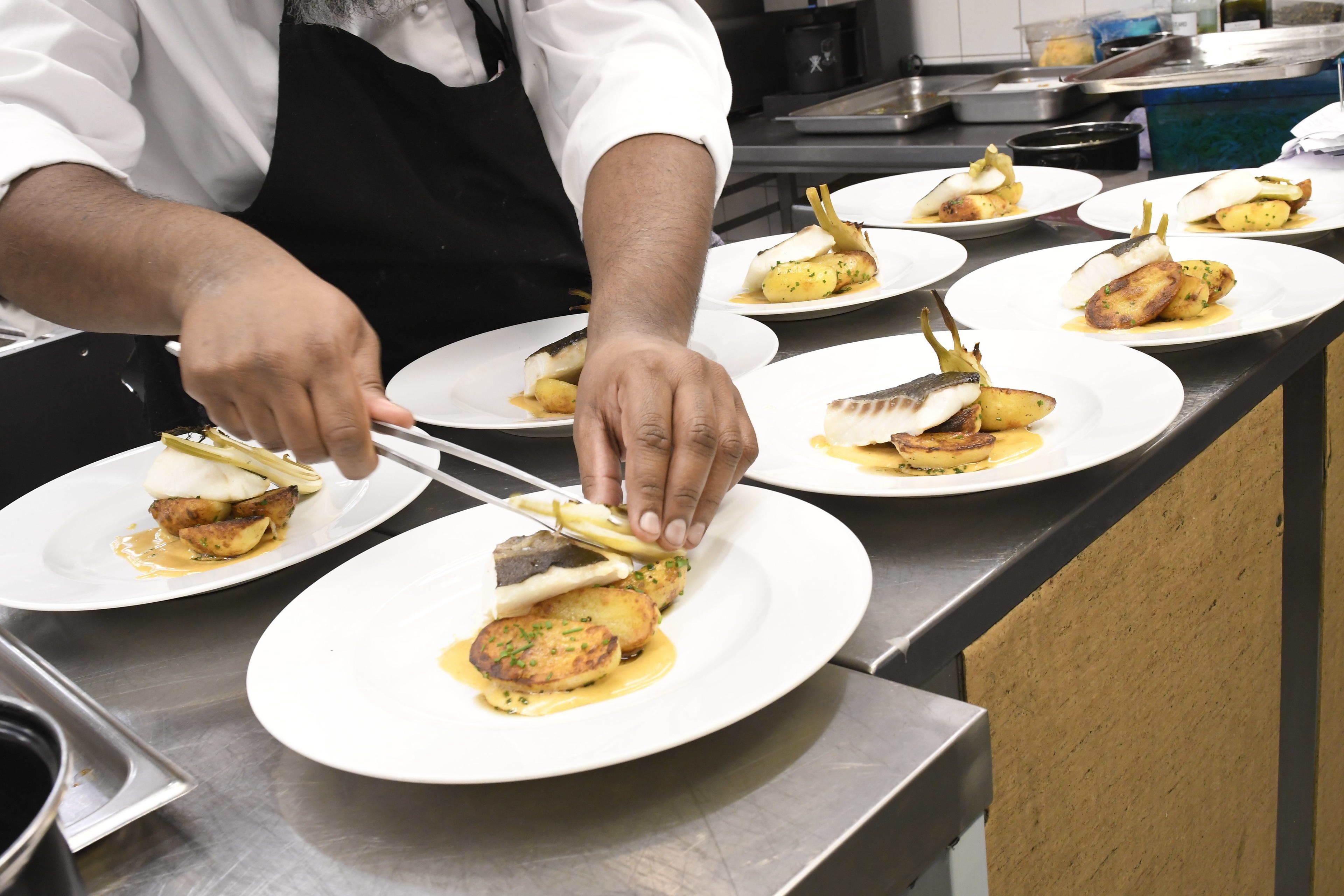 A chef plating dishes on white plates.