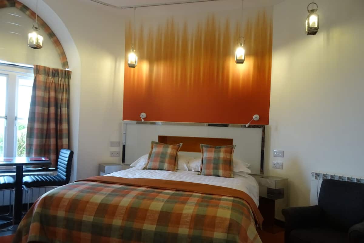 Quarto de hotel com uma cama grande, duas luminárias de cabeceira, cabeceira e uma janela com cortinas.