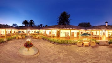 Un hotel con varias habitaciones, un patio central con una fuente, zona de estar al aire libre y tejado de baldosas.