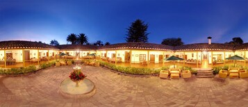 Un hotel con varias habitaciones, un patio central con una fuente, zona de estar al aire libre y tejado de baldosas.