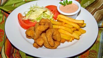 A plate of food including fried items, French fries, a salad, and a small bowl of sauce.