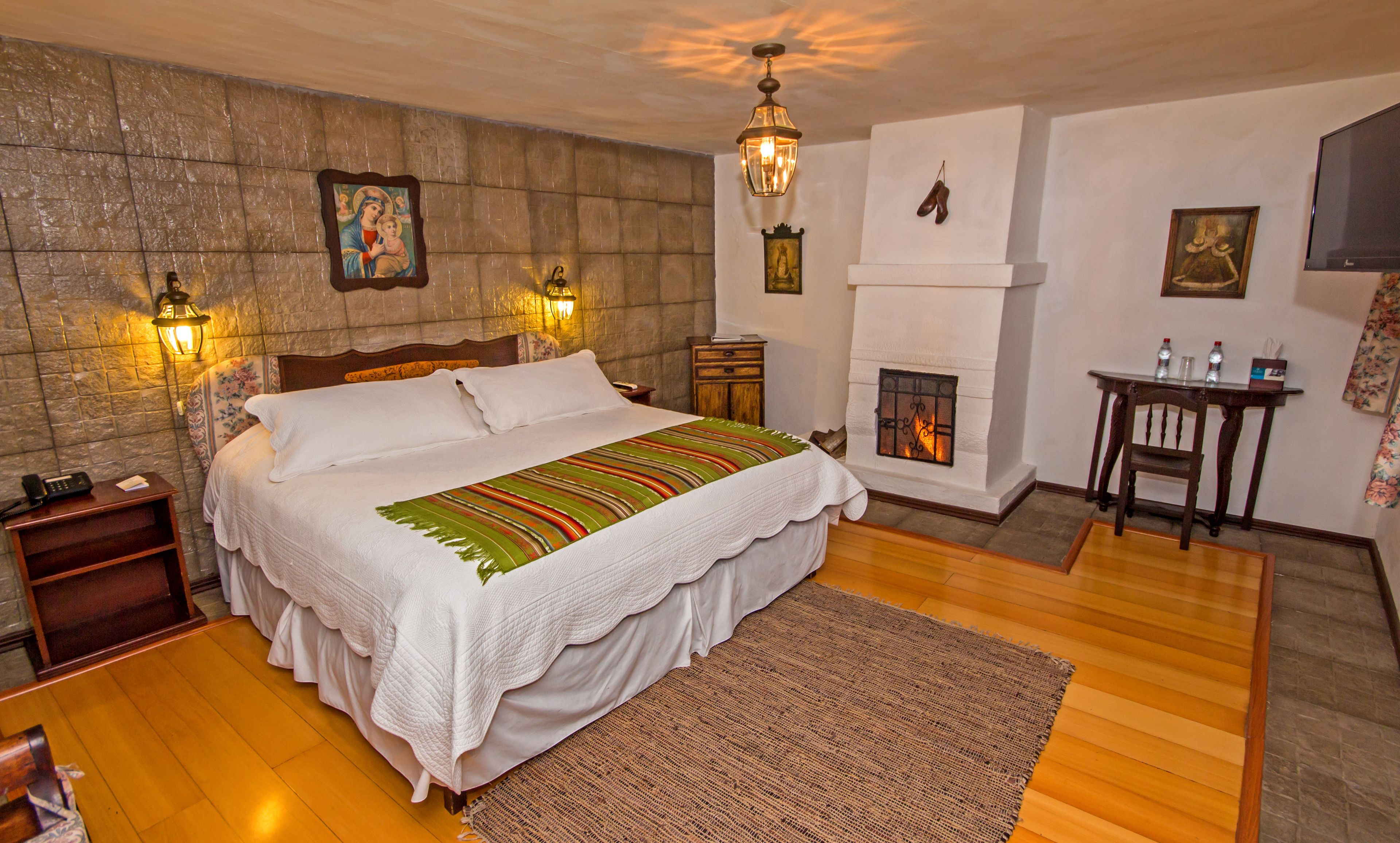 A well-appointed bedroom with a large bed, a fireplace, and a nightstand with a lamp.