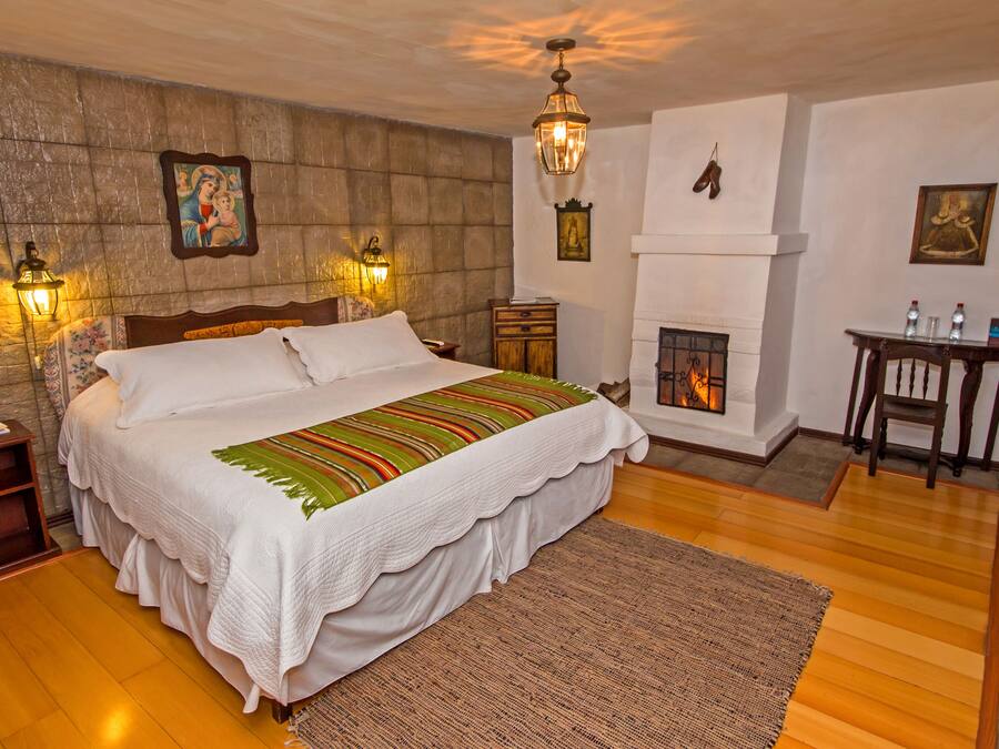 A well-appointed bedroom with a large bed, a fireplace, and a nightstand with a lamp.