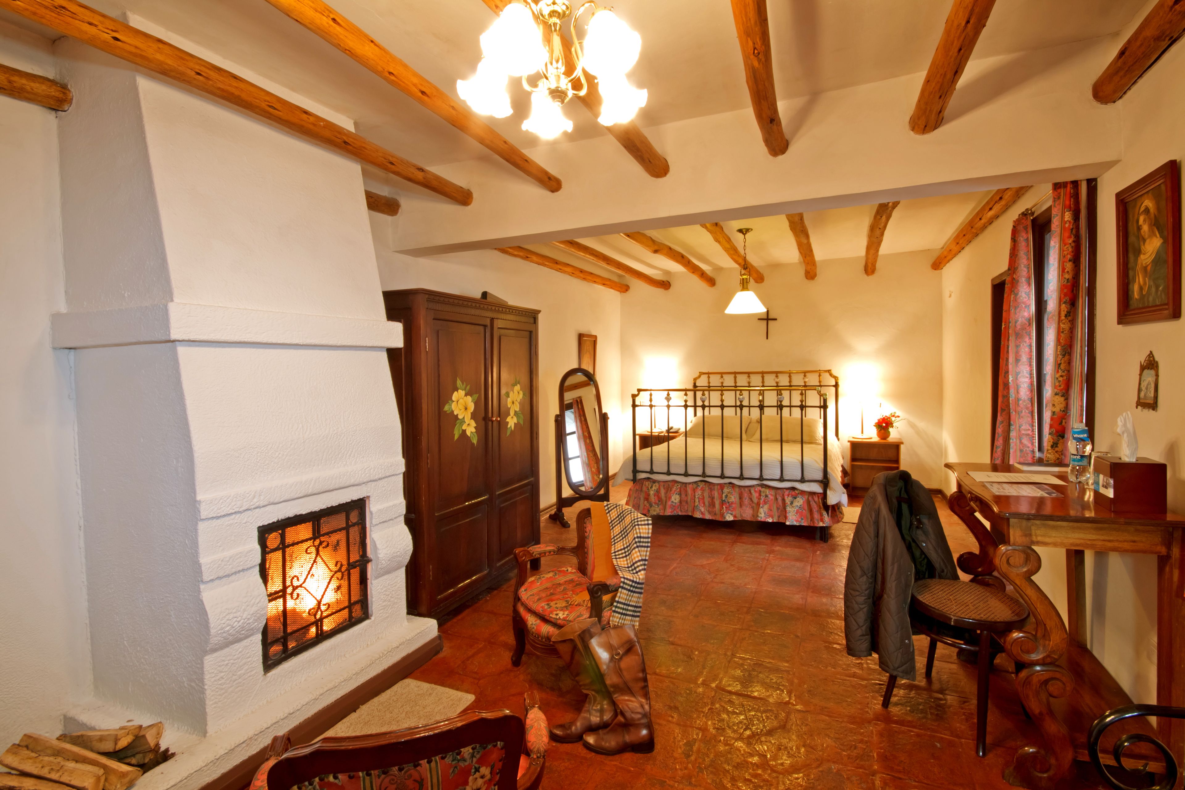 A traditional room with a fireplace, wooden beams, a wooden chair, a table, and a bed with a floral bedspread.