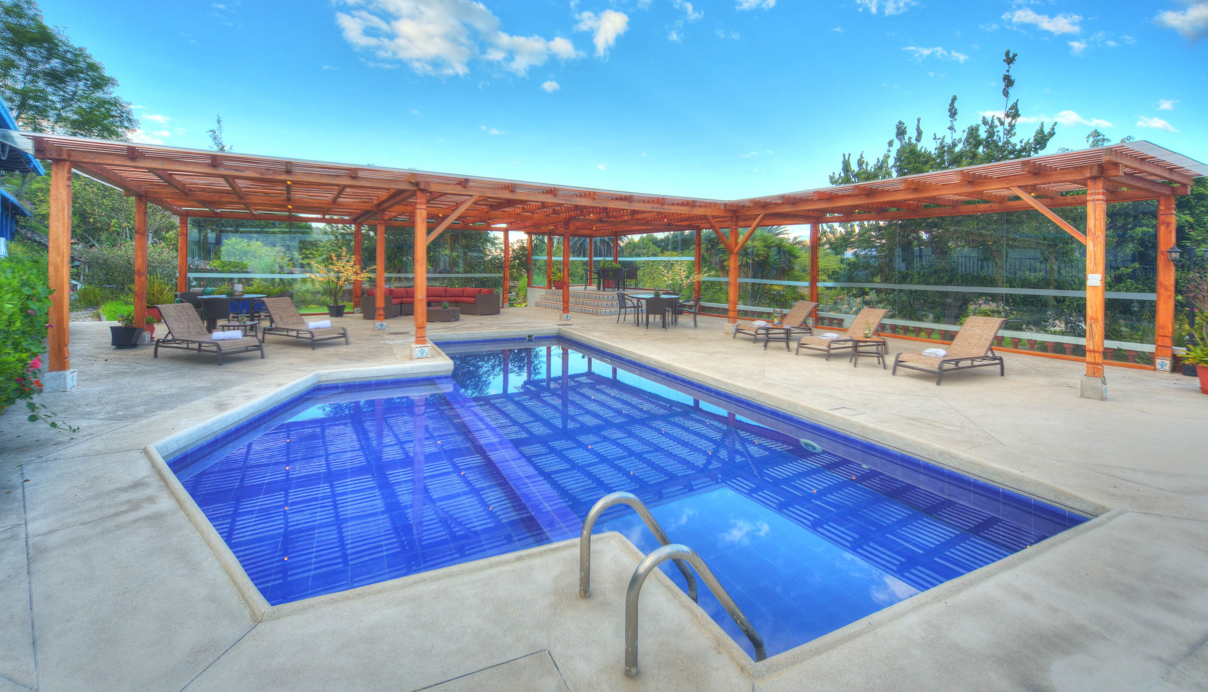 Piscina com pergolado de madeira, espreguiçadeiras e vista para o verde.