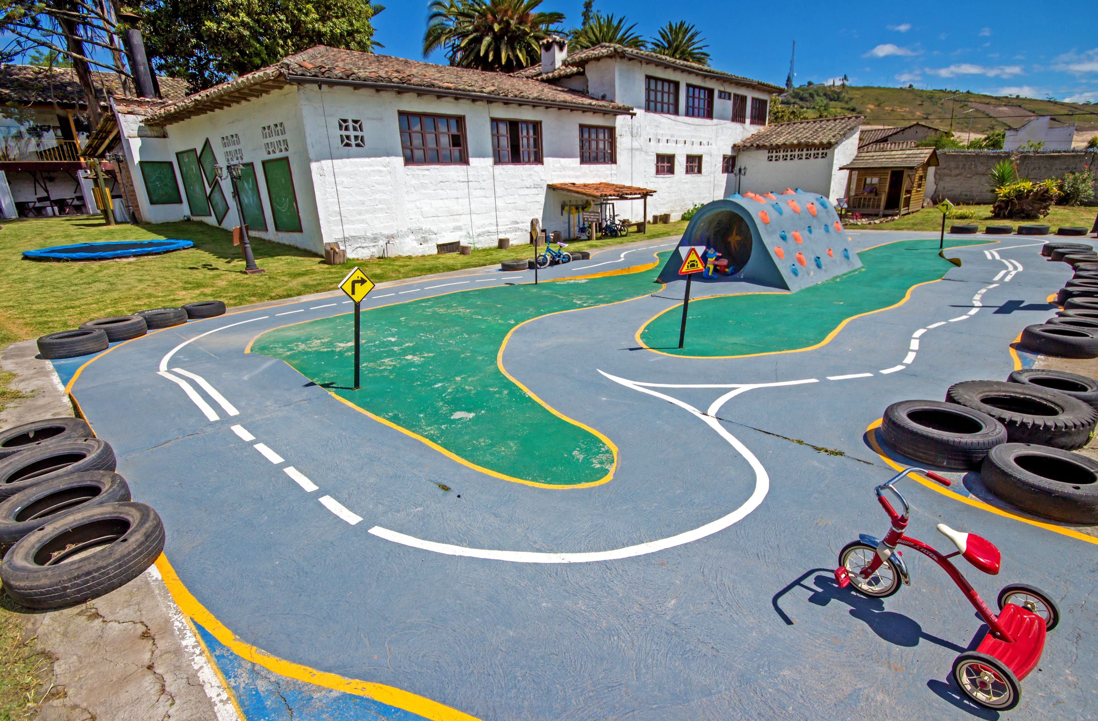 Une aire de jeux avec un chemin sinueux, un mur d’escalade et un tricycle rouge.