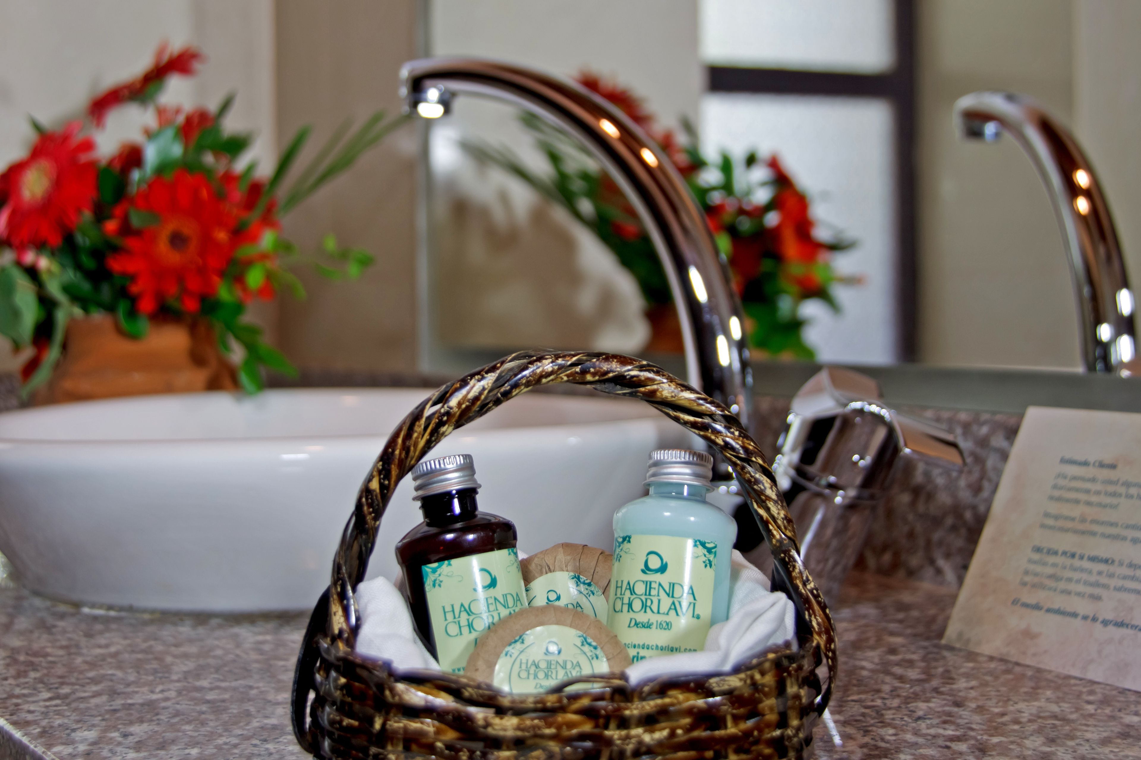 A bathroom sink with a mirror, a faucet, and a basket containing three bottles of toiletries.