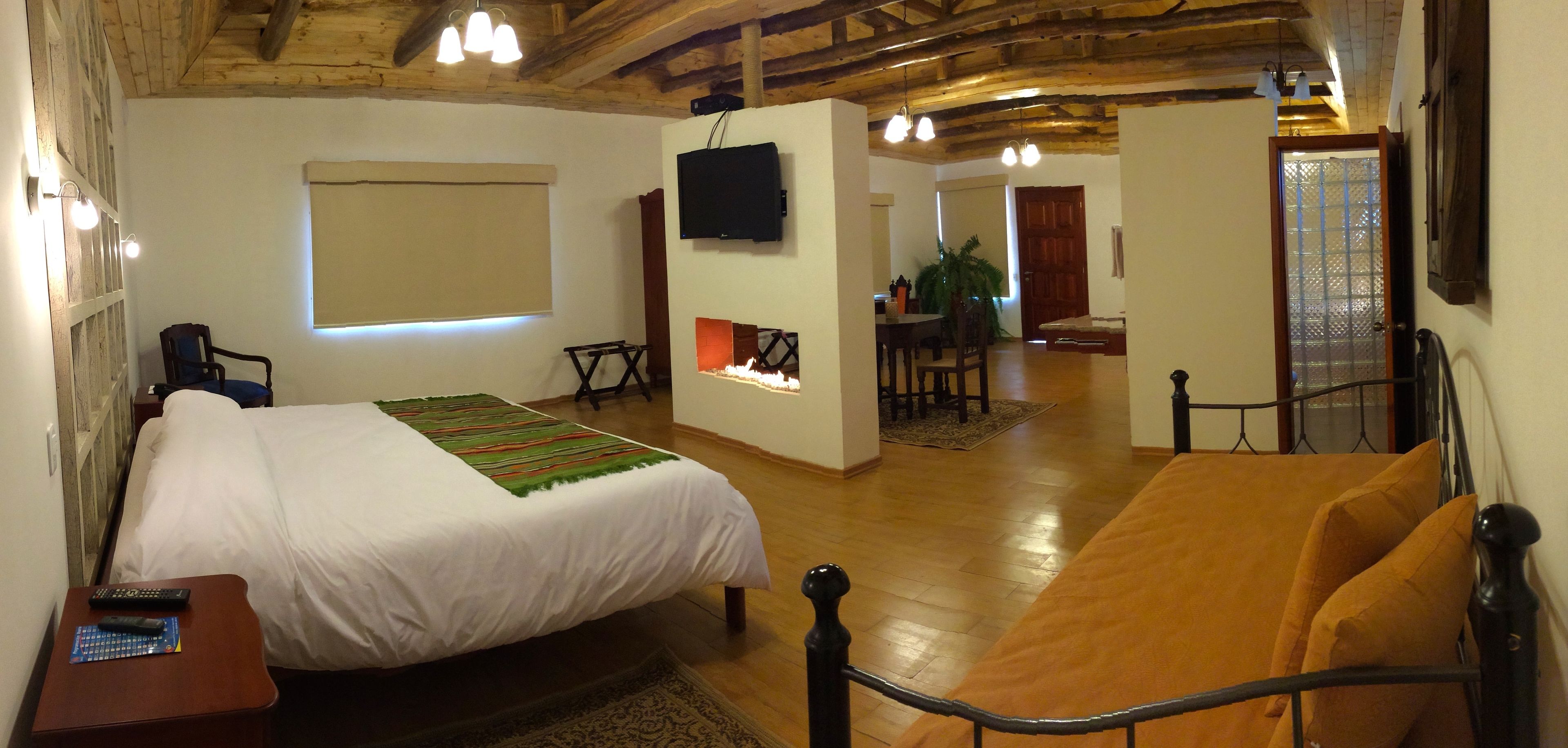 A bedroom with a bed, a sofa, a TV, and a fireplace.