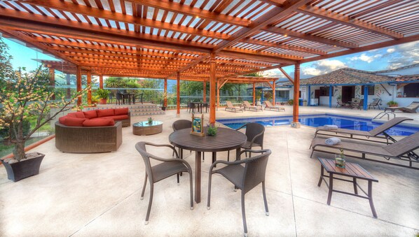 An outdoor patio with a pool, wooden pergola, wicker furniture, and a red sofa. - Hacienda Chorlavi (Ibarra)