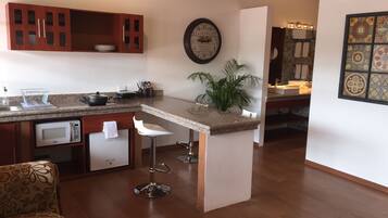 Een moderne keuken met een centraal eiland, barstoelen, een magnetron en een klok aan de muur.