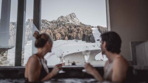 Two people in a hot tub with a view of a snowy mountain and a ski lift. - Hotel Continental Dolomites (Selva di Val Gardena)