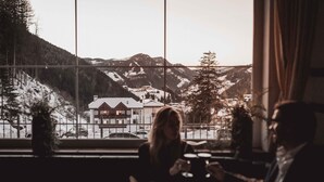 A dining area with a view of snow-covered mountains and a building in the distance. - Hotel Continental Dolomites (Selva di Val Gardena)