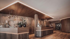 A reception area with wooden reception desks, a wooden ceiling, and a modern light fixture. - Hotel Continental Dolomites (Selva di Val Gardena)