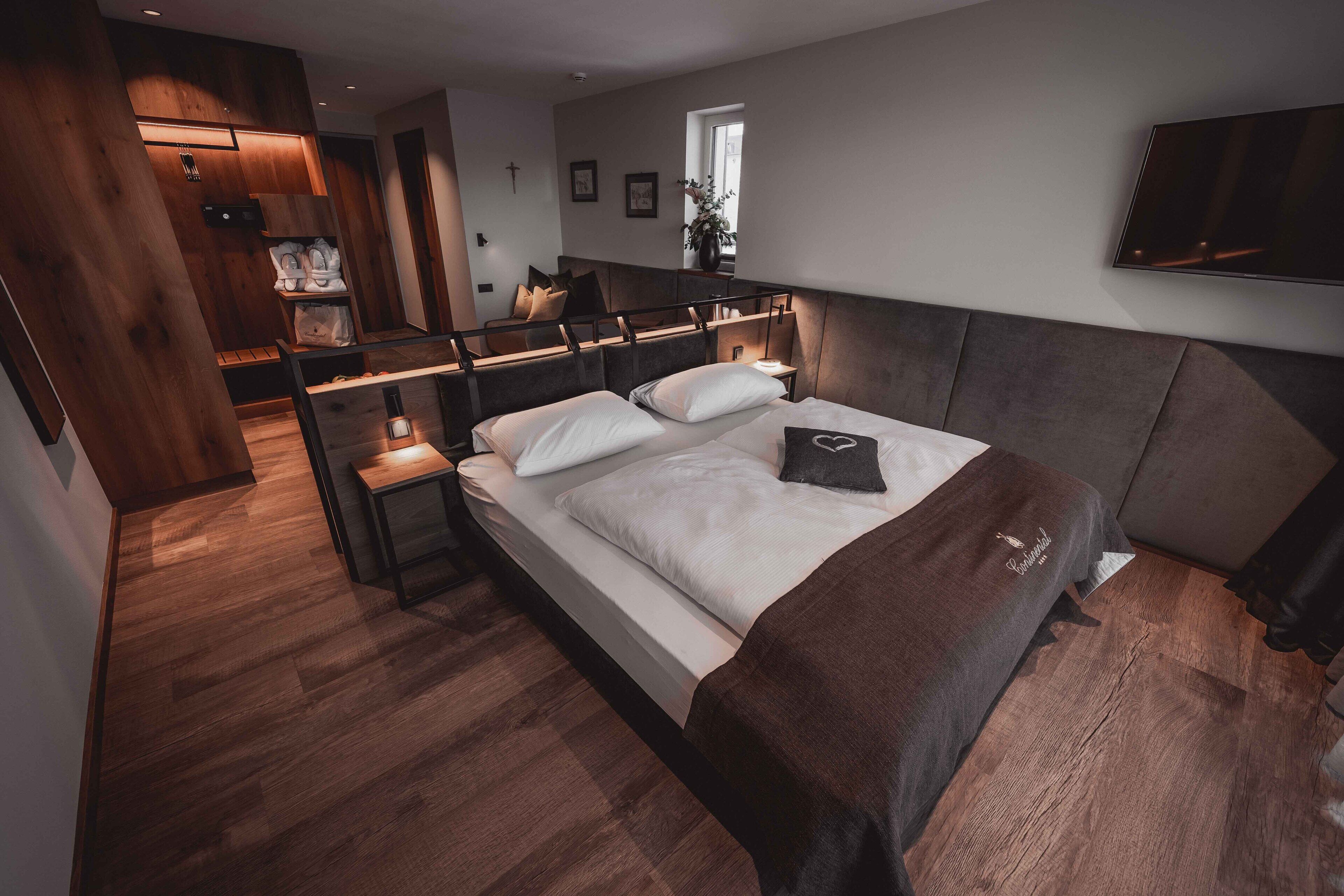 Una camera da letto moderna con un letto grande, pavimento in legno, una panca integrata e una TV a parete.