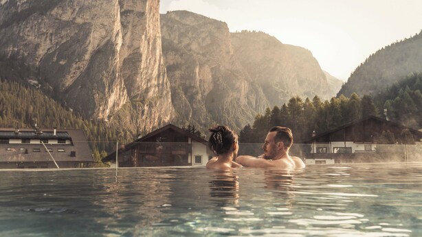 A couple in a swimming pool with a mountainous backdrop. - Hotel Continental Dolomites (Selva di Val Gardena)