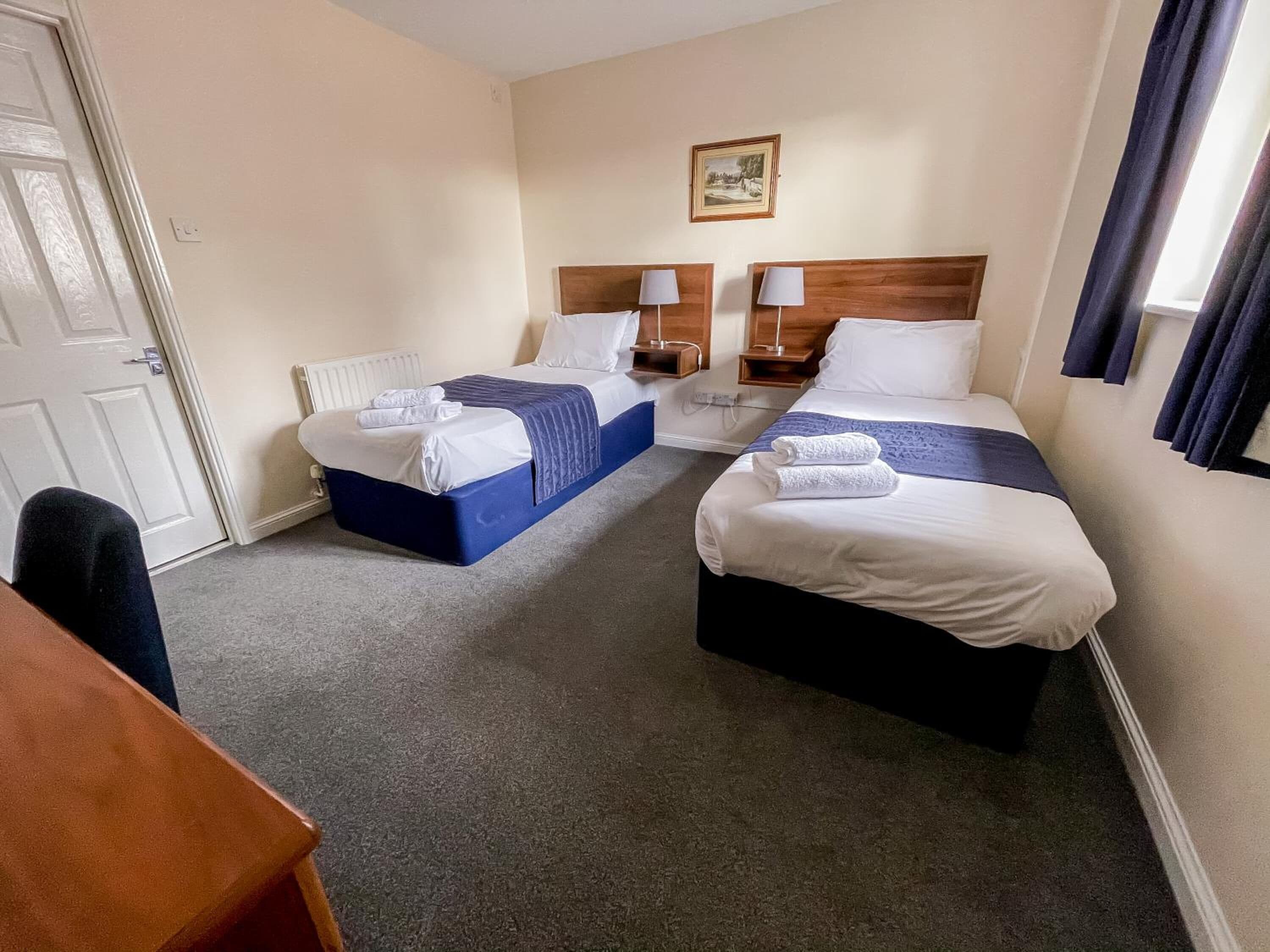 A hotel room with two beds, a wooden headboard, a small table, and a painting on the wall.