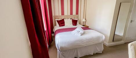 Una camera d'albergo con un letto, un comodino, una lampada, uno specchio e una porta.